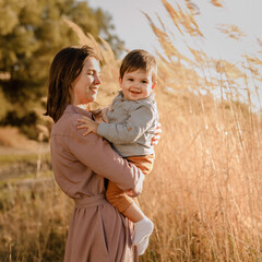 Portrait of happy loving mother hugging her baby son in the sunny park near river