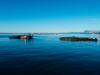 man working on fish farm with ponds nets boats at sea with mountain background