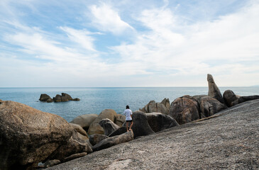 Naklejka premium Young Man with a long hair in a white t-shirt, standing on a rock and enjoying a view on a sea. Traveling.