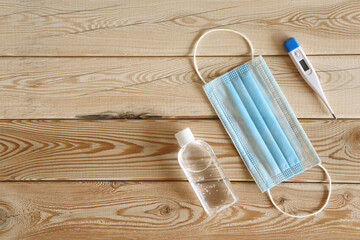 blue mask, antiseptic and thermometer on wooden background COVID-19
