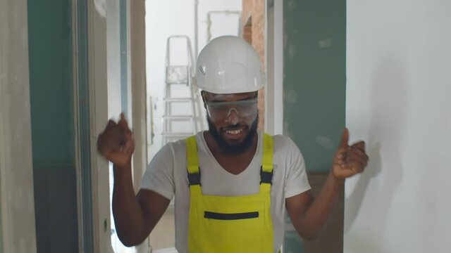 Portrait of happy african builder man in uniform dancing and smiling doing house renovation