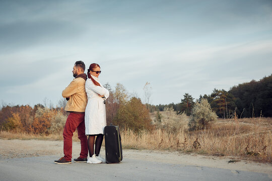 traveling man and woman with a suitcase on an empty road, travel concept