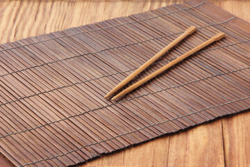 Sushi sticks on brown bamboo food placemat on wooden table.