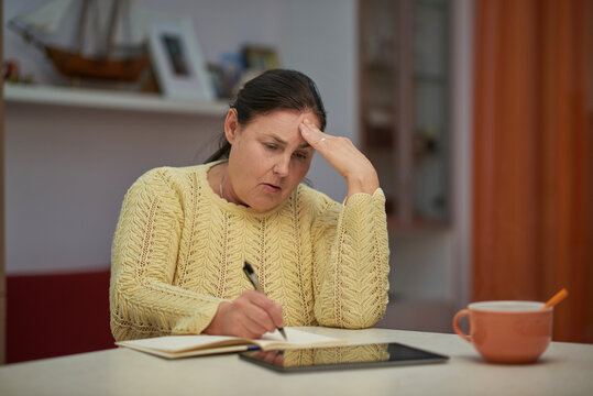 Worried senior woman in yellow sweater writing