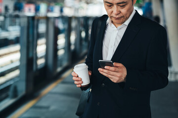 Handsome business man holding a disposable coffee cup and using phone at train station