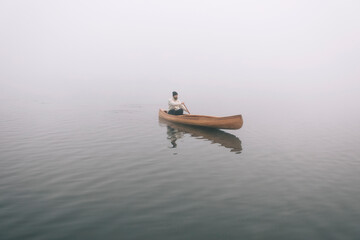 Winter canoeing. Man paddling canoe on the foggy lake