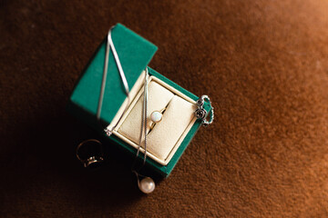 Open bottle-green jewelry box with rings and pearl necklace.