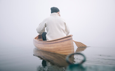 Man paddling canoe on the foggy lake