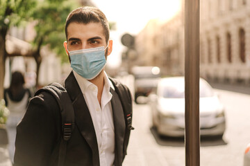 Man in suit waiting at the bus stop wearing a protective mask. Coronavirus lifestyle concept.