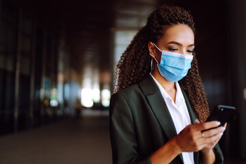 Beautiful businesswoman in medical protective mask using the phone. Safety during coronavirus...