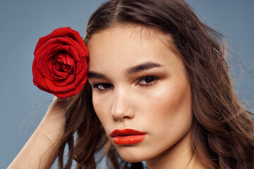 Fototapeta na wymiar Woman portrait with red rose near the face on gray background and makeup curly hair