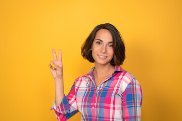 Young woman shows the sign of peace by her hands on yellow background. High quality photo