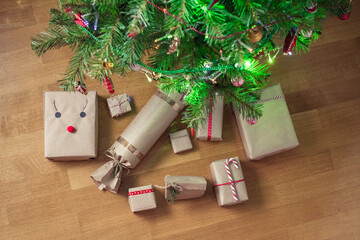 Santa Claus putting handmade gift wrapping in a craft paper under christmas tree. Presents for family. Top view. Flat lay.