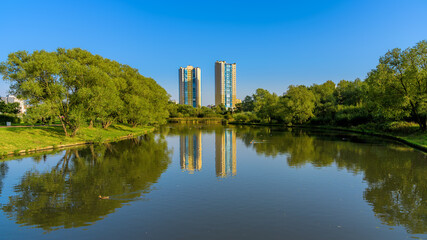 Fototapeta na wymiar High multi-storey residential buildings are reflected in the calm water of the pond at sunny autumn day