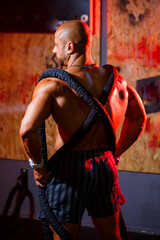 Sporty handsome strong man posing with sports rope on the background of the gym. A strong bodybuilder with perfect abs, shoulders, biceps, triceps and chest.