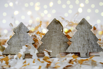on a light background with bokeh among confetti is three wooden Christmas trees. Christmas decorations