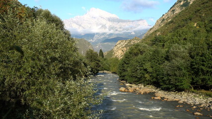 Fototapeta na wymiar The blue mountain river flows against the background of a snowy mountain. Travel to the mountains.