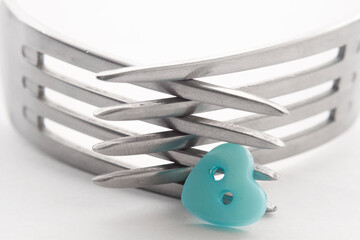 Closeup of the crossed tines of two forks. Next to it is a blue button in the shape of a heart . White background, selective focus