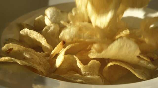 Potato Chips fall into white plate in slow motion close up