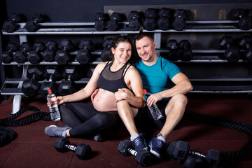 Fototapeta na wymiar Pregnant woman goes for sports with her husband in gym for cross training. Couple athletes expecting baby while resting after training and exercises to strengthen health and muscles expectant mother