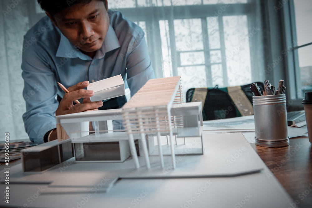 Poster asian architect-designer holding the part of the model of modern box house while thinking about conc