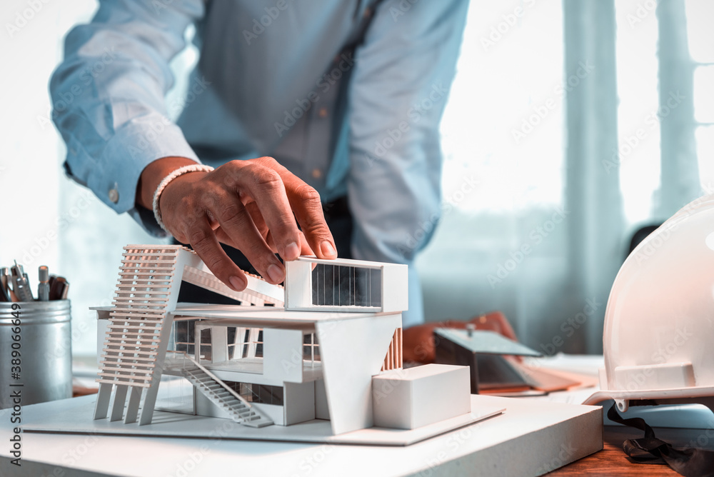 Poster hand of asian architect-designer holding the part of the model of modern box house while thinking ab