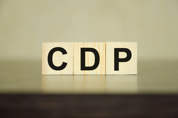 the word is written on wooden cubes, in the background is a calculator on a financial chart. The word CDP is present. This stands for Customer Data Platform.