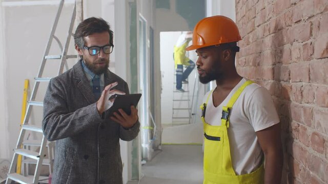Worker and client using tablet pc at construction site planning renovation