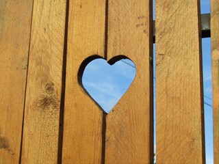 Brown colour wooden fence with heart shaped hole and blue sky 