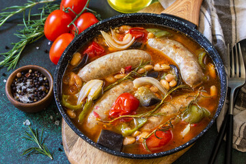 Stew smoked sausages with of beans, vegetables and tomato sauce in the pan on a stone countertop.
