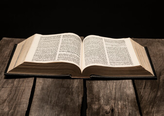 Holy bible open on rustic wooden table in dark night.