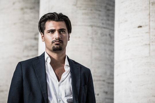 Portrait Of Young Man With Trendy Style. Trendy Hair And Goatee. He Wears A White Shirt And Jacket.