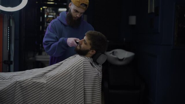 A bearded man trims his beard in a barber shop. Barber works as a trimer in a salon