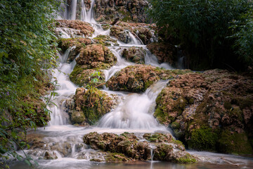 Small waterfall among the vegetation pouring water into a lake, Orbaneja del Castillo, Burgos, Spain