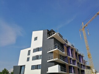 New multi-storey apartment building with a white and gray facade, with balconies, next to which stands a construction crane