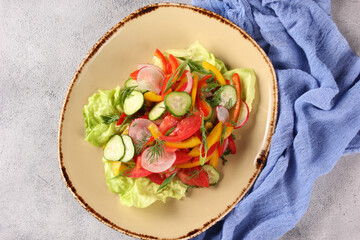 Salad of fresh vegetables: tomatoes, cucumbers, radish, sweet peppers, red onions and herbs in a beige plate on a gray table. Restaurant menu. Restaurant menu. Background image. Top view, flatlay