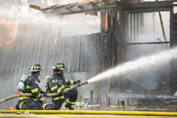 A residential home burns in a house fire as firefighters spay water from a hose in an effort to put...
