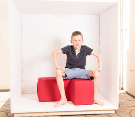 Boy sitting on a red stool in a box