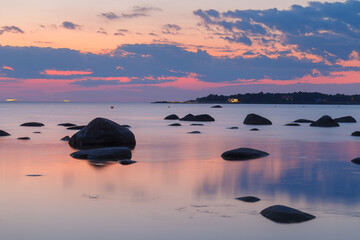 Fototapeta na wymiar Romantic sunset at sea. Big boulders sticking out from smooth wavy sea. Pink horizon.