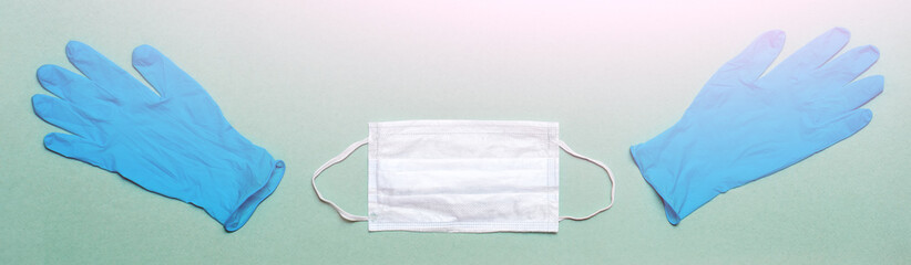A pair of thin blue medical latex gloves and medical face mask on a green background. Disposable rubber medical gloves and mask. Protective subjects. Remedies. Top view.