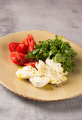 Italian cuisine. Caprese. Mozzarella, tomatoes and arugula with pesto sauce and olive oil in a beige plate on a gray background.Restaurant menu. Background image, copy space. Flatlay, top view