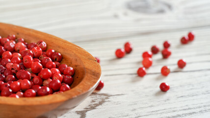 Red or Pink peppercorn in small wooden bowl, some scattered on white boards desk, closeup detail