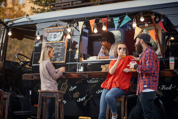 people socializing in front of truck food, drinking juices, talking
