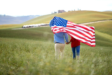 A couple in love walking the meadow holding the American flag. Election, campaign, freedom concept