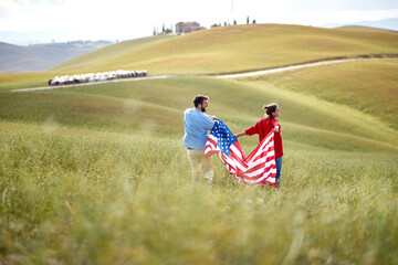 A couple in love holding the American flag at a meadow. Election, campaign, freedom concept
