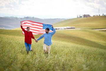 A couple in love running a meadow with unfurled American flag above heads holding by hands. Election, campaign, freedom concept