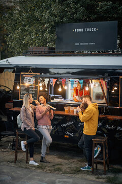 vertical image of multiethnic young people socializing while eating outdoor in front of modified truck for fast food