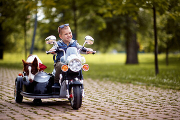 Happy little boy driving a toy motorcycle with his dog