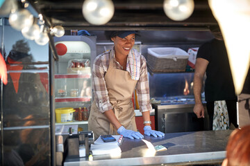 friendly afro-american female employee in street fast food service, food truck concet