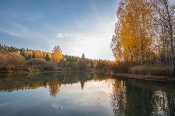 Autumn landscape, a beautiful forest on the banks of the river, the sunlight and the rays through yellow, gold foliage. Bright colors of autumn on the trees.